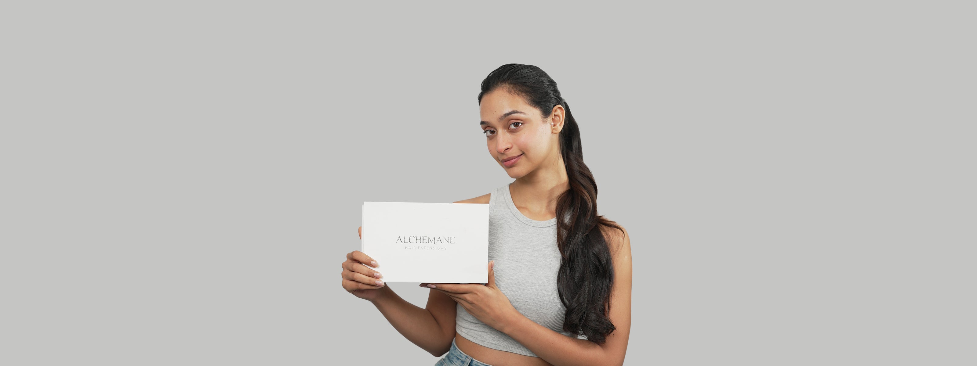 "Smiling woman holding an Alchemane Hair Extensions box, showcasing premium hair solutions for enhanced volume and style."