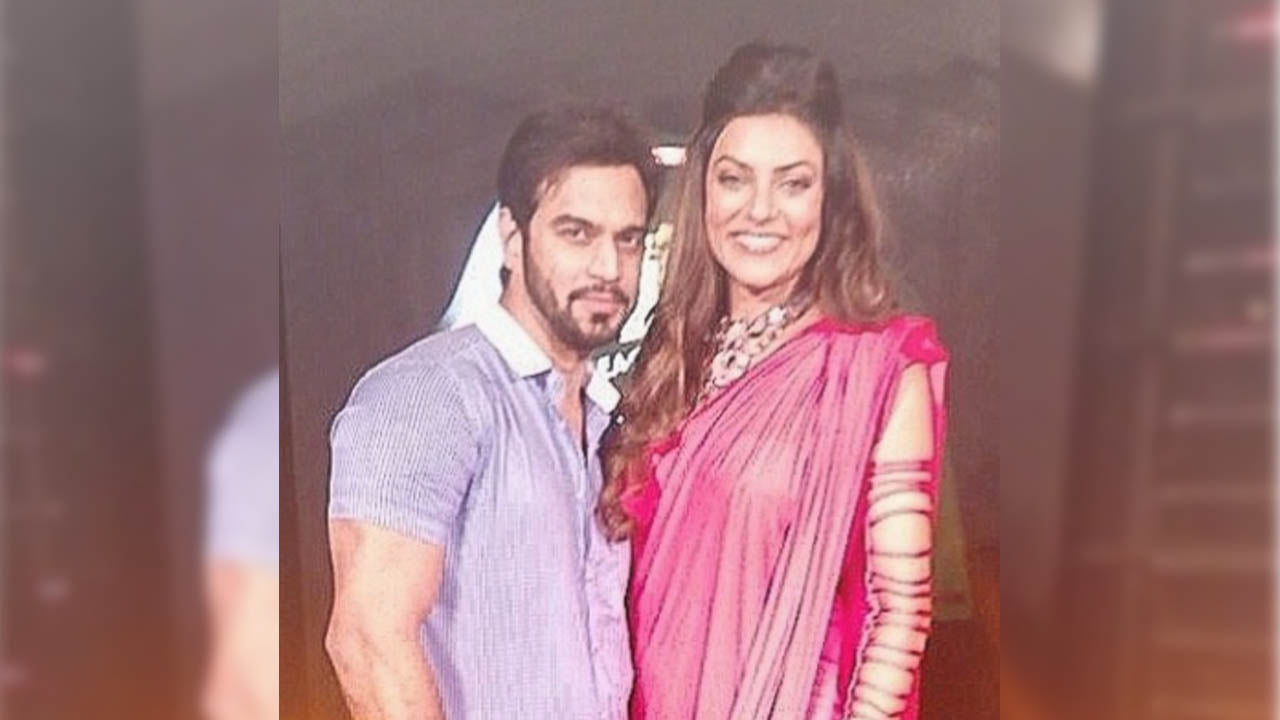 "A man in a casual blue shirt and a woman in a vibrant pink saree posing together at an event, both smiling at the camera."