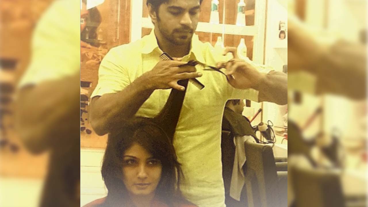 "A professional hairstylist in a yellow shirt carefully trimming a woman's hair in a well-lit salon, with salon products and other clients visible in the background."